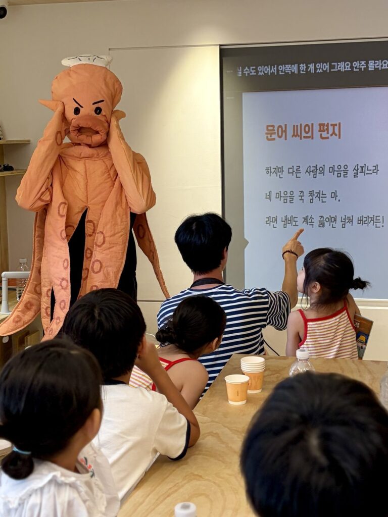 2026년 8월 29일 MR.팬지 작가 북토크와 라면 파티 — 문어 인형 옷을 입은 작가가 '문어 씨의 편지' 화면 앞에서 어린이들과 이야기해요