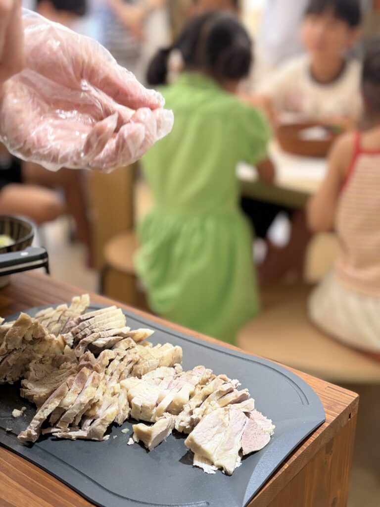 2026년 8월 29일 MR.팬지 작가 북토크와 라면 파티 — 도마 위에 썰어 놓은 고기, 뒤로 어린이들이 앉아 기다리고 있어요