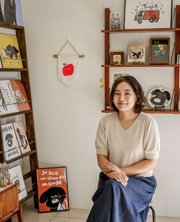 책과 그림이 놓인 작업실에 앉아 미소 짓는 윤나리 작가